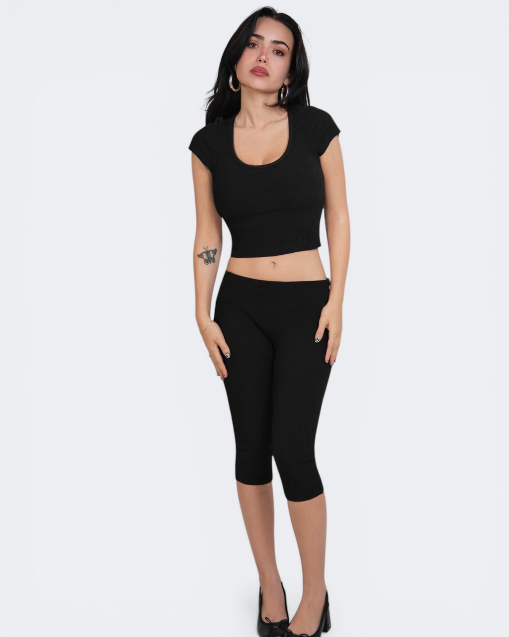 Woman wearing a black crop top and capri leggings on a white background