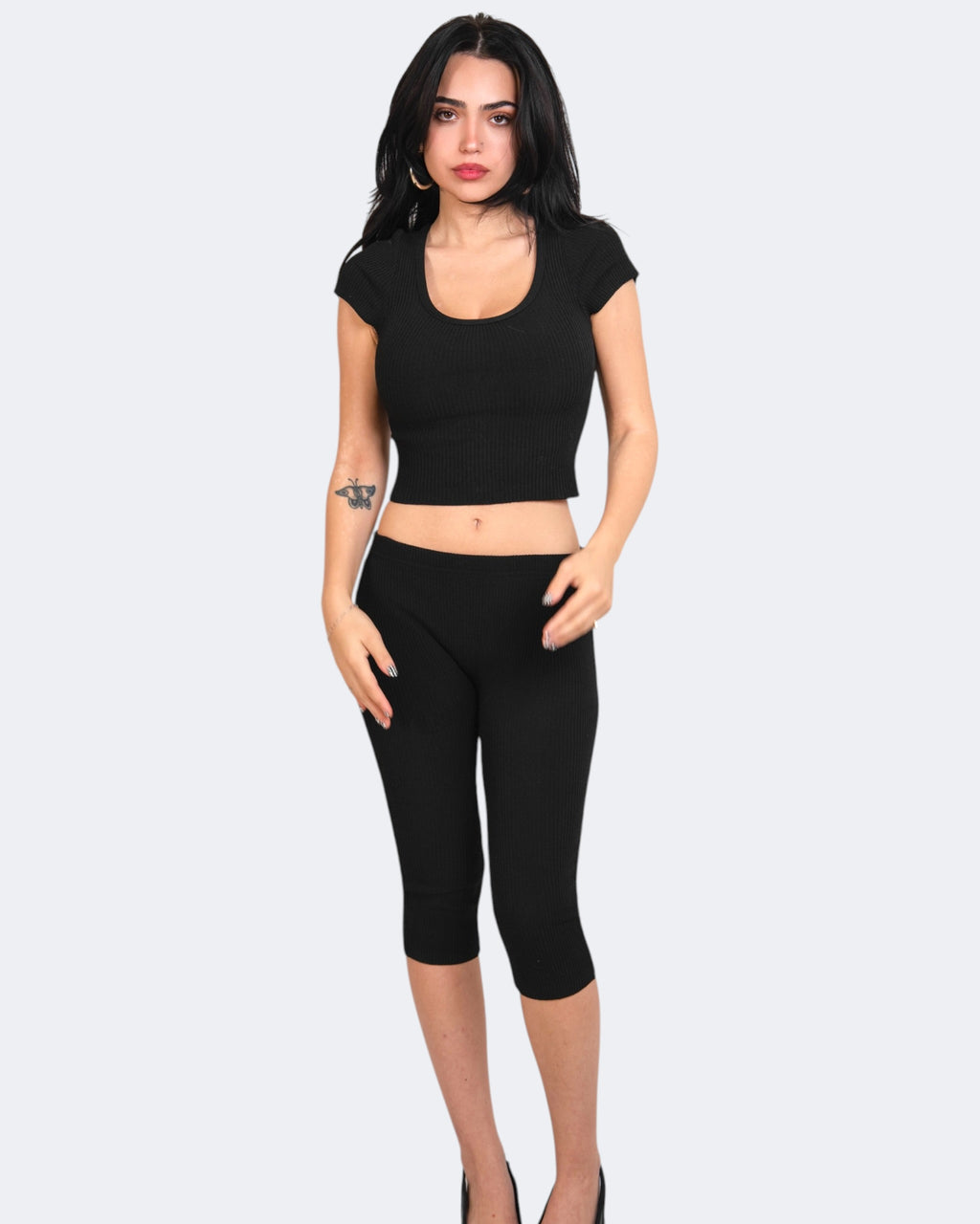 Woman wearing a black crop top and capri leggings on a white background
