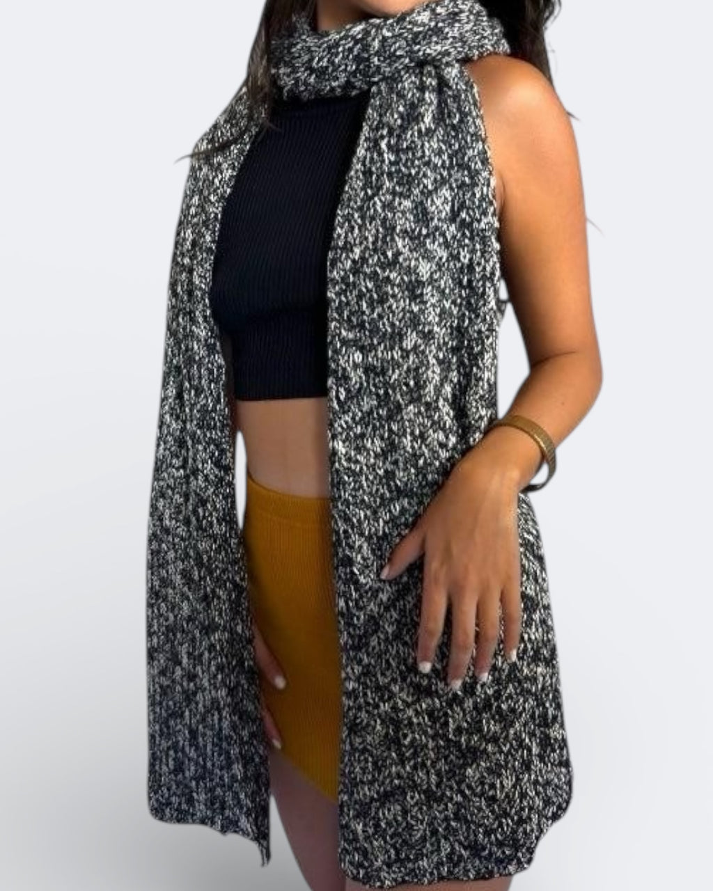 Person wearing a long, black and white patterned scarf by the Knit House LA, with a plain background