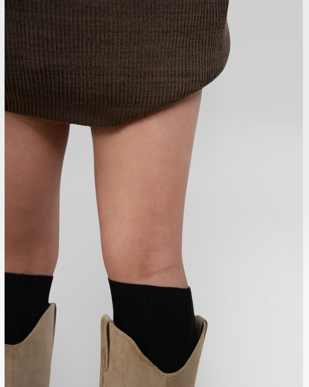 Person wearing brown boots and black socks on a plain background