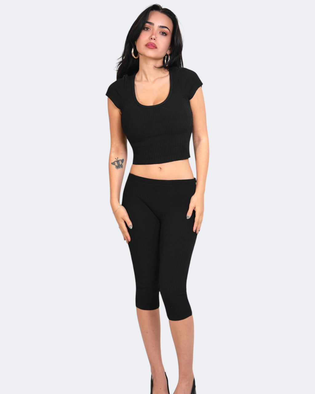 Woman wearing a black crop top and capri leggings on a white background