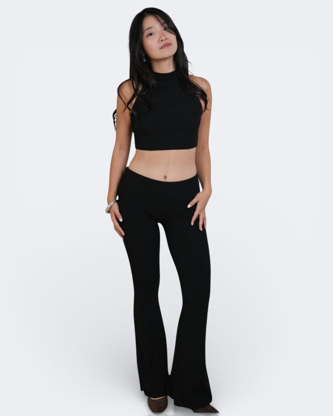 Woman wearing a black crop top and black flared pants on a white background