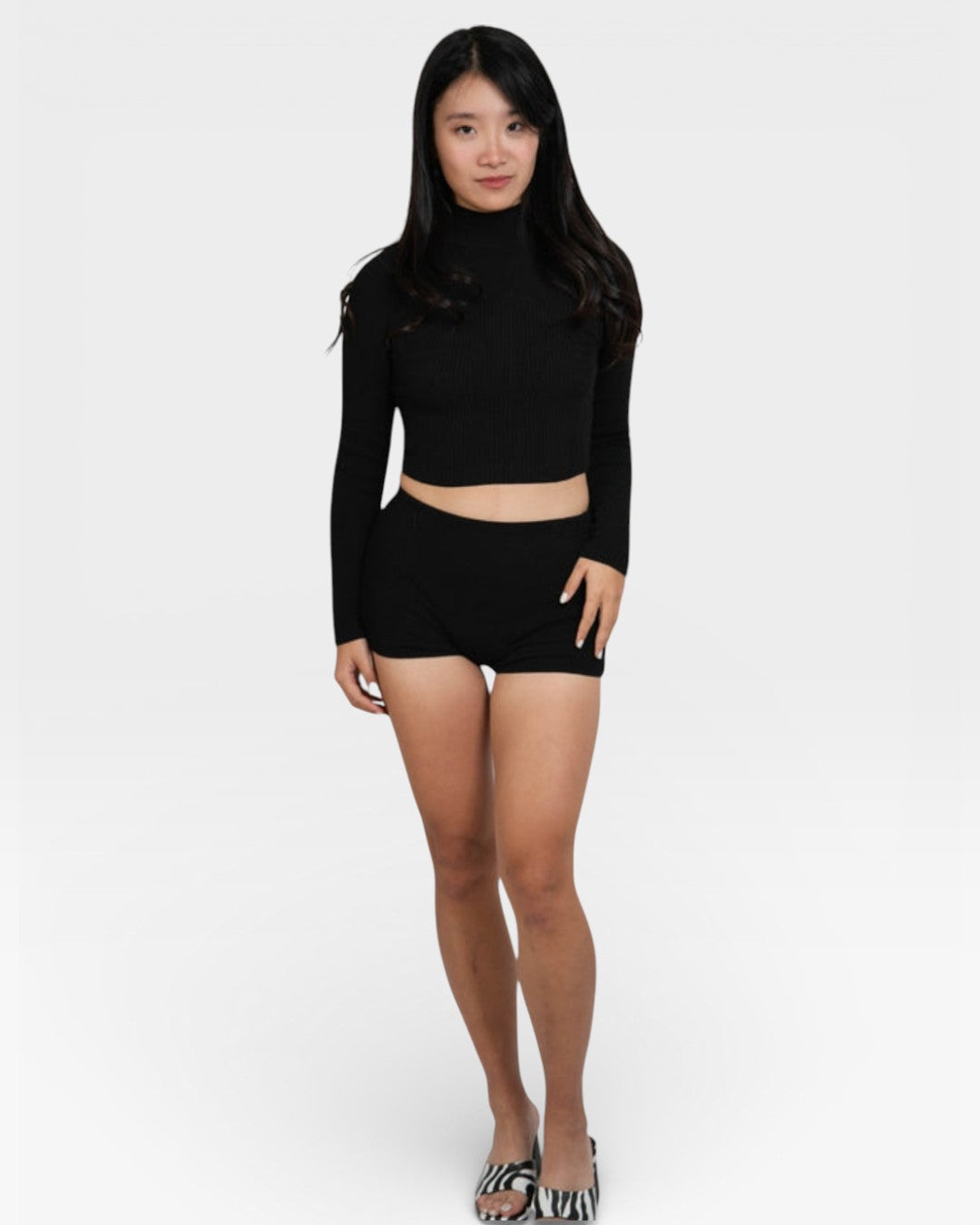 Person wearing a black long-sleeve top and black shorts on a white background