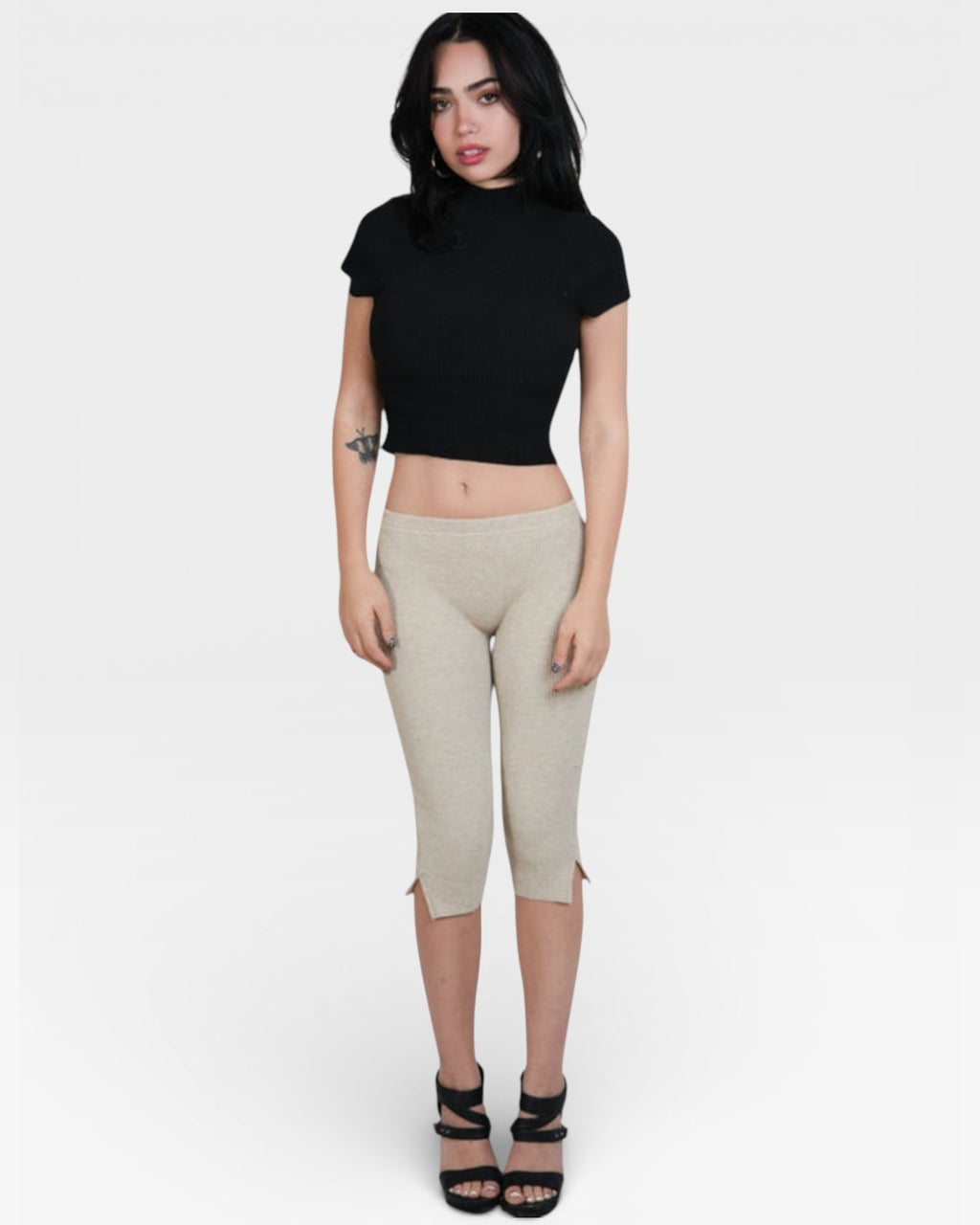 Woman wearing a black crop top and beige capri pants on a white background