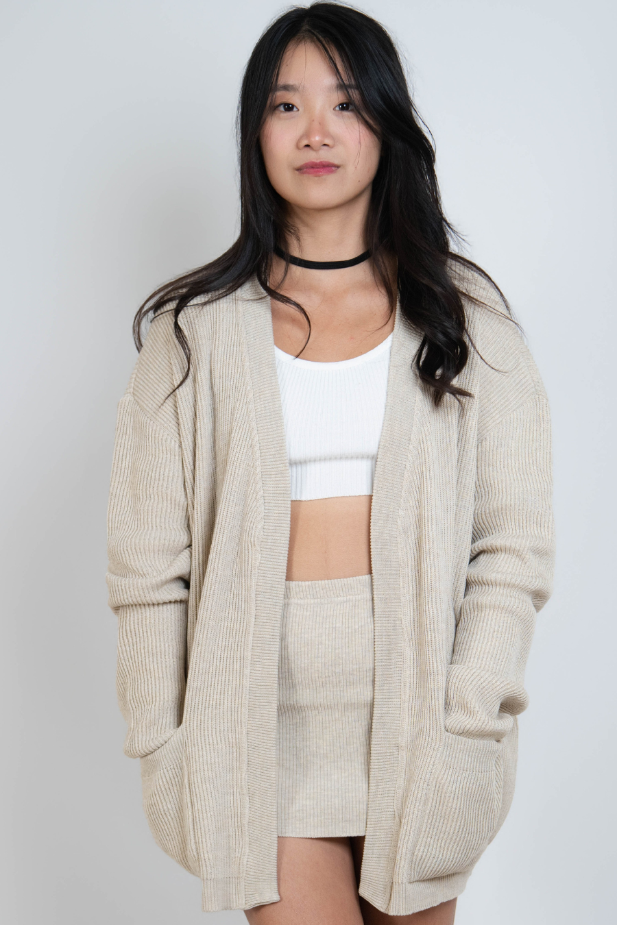 Woman wearing a neutral beige cardigan over a white top and drift beige skirt  by The Knit House LA